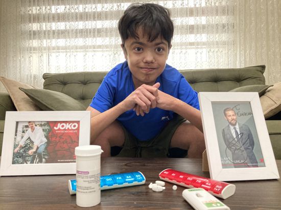 Ein junger Mann in blauem T-Shirt sitzt hinter den Bildern von Joko und Klaas und hat diverse Medikamente vor sich ausgebreitet. 