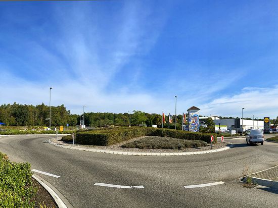 Panoramabild mit blauem Himmel, Kreisel, Autos, im Hintergrund Gewerbe und Wald