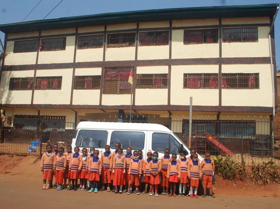 Kinderschar in Kamerun vor Spendenbus stehend der vor Gebäude parkt 