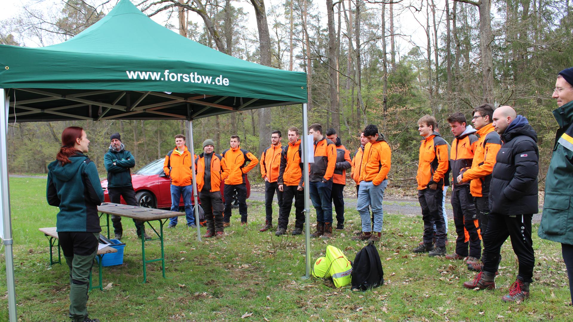 Yvonne Hengst spricht zu orange gekleideten Forstwirt-Azubis über die Ansprache von Waldbesuchern. 