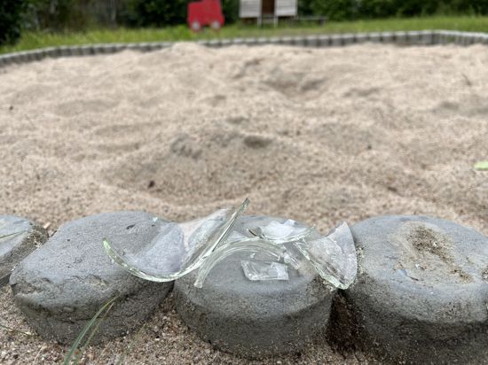 Glasscherben liegen auf der steinernen Begrenzung eines Sandkastens. 