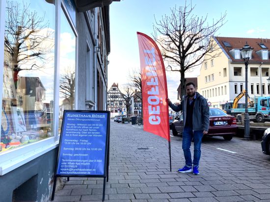 Christopher Böser steht mit einer roten Fahne, auf der „Geöffnet“ steht, vor seinem Kunsthaus in der Weingartener Bahnhofstraße. 