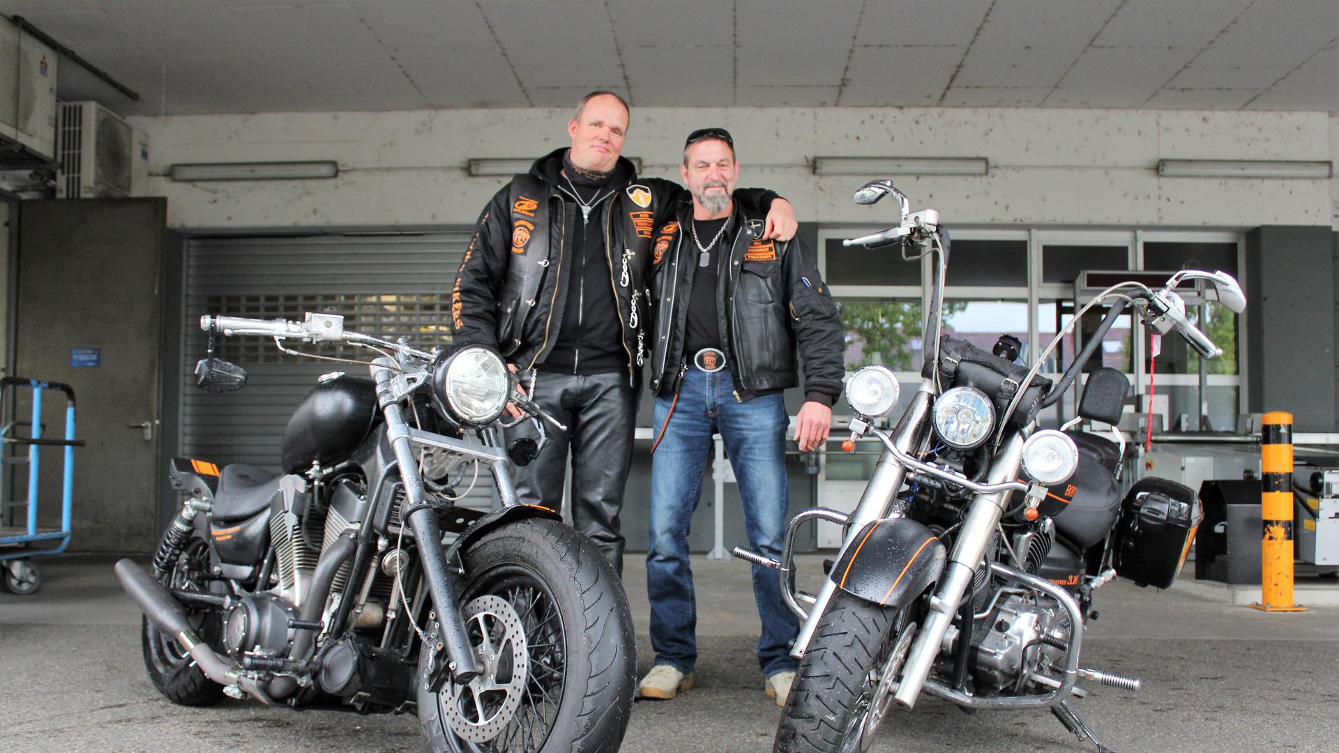 Andreas Dörr (links) und Oliver Bodrogi stehen in Newborn-Bikers-Jacke und Kutte neben ihrem Motorrädern. 