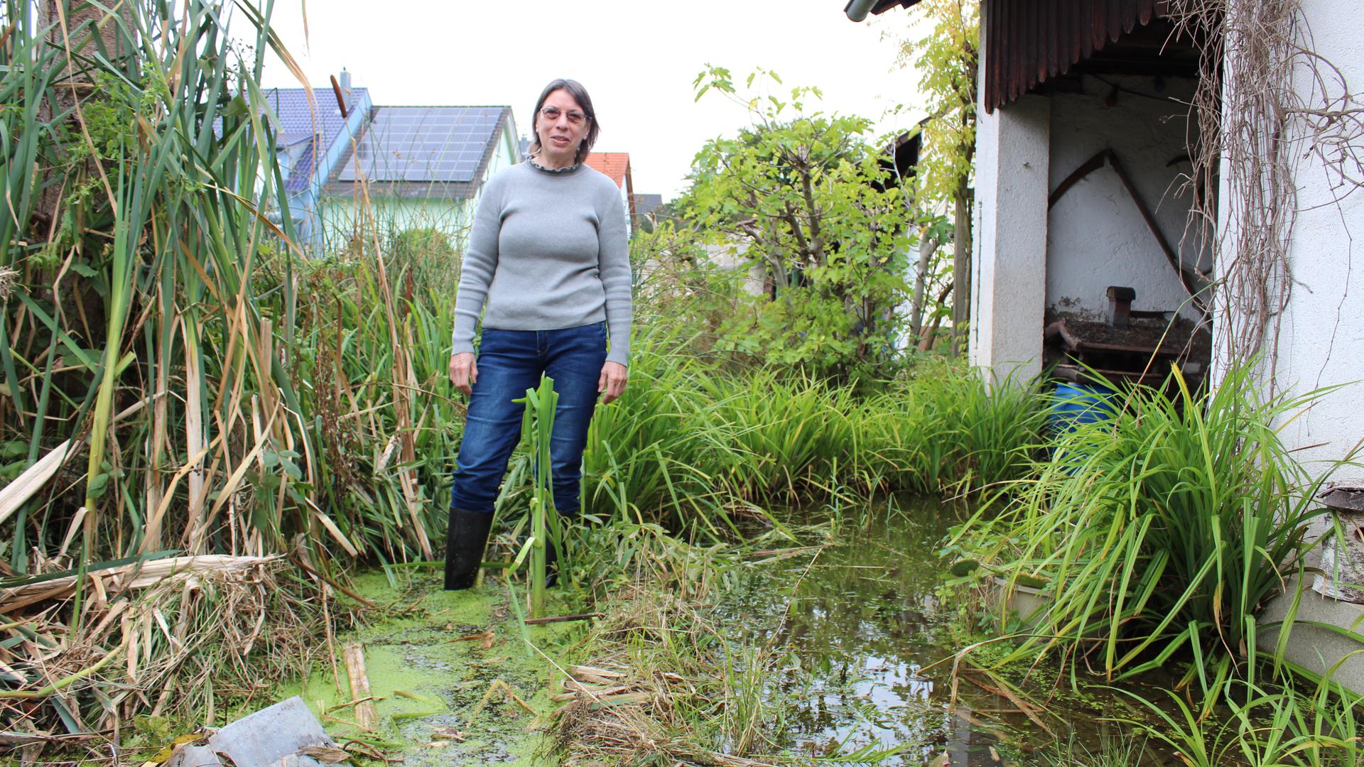 Edeltraud Malsch steht mit Gummistiefeln knöcheltief im Wasser in ihrem Garten. 