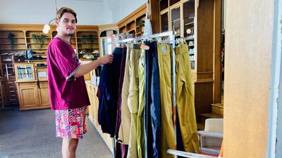 In 80er Boxershorts und weitem T-Shirt steht Lennard Bauer an einem Kleiderständer des Vintage Ladens für den er arbeitet.
