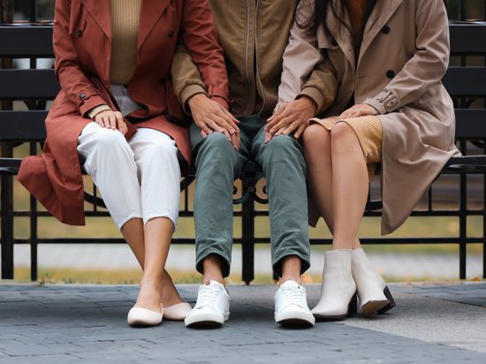 Liebe zu dritt: Ein Mann und zwei Frauen sitzen auf einer Bank und halten sich an den Händen.