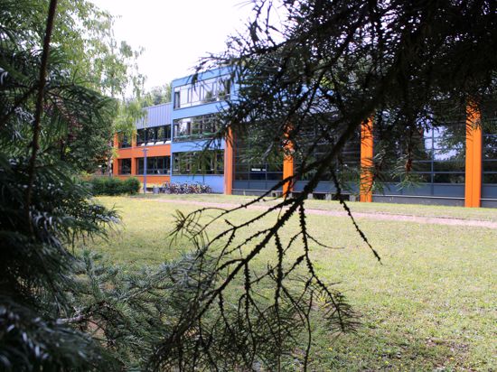 Ein Schulgebäude in Blau und Orange ist hinter einer grünen Wiese zu sehen.