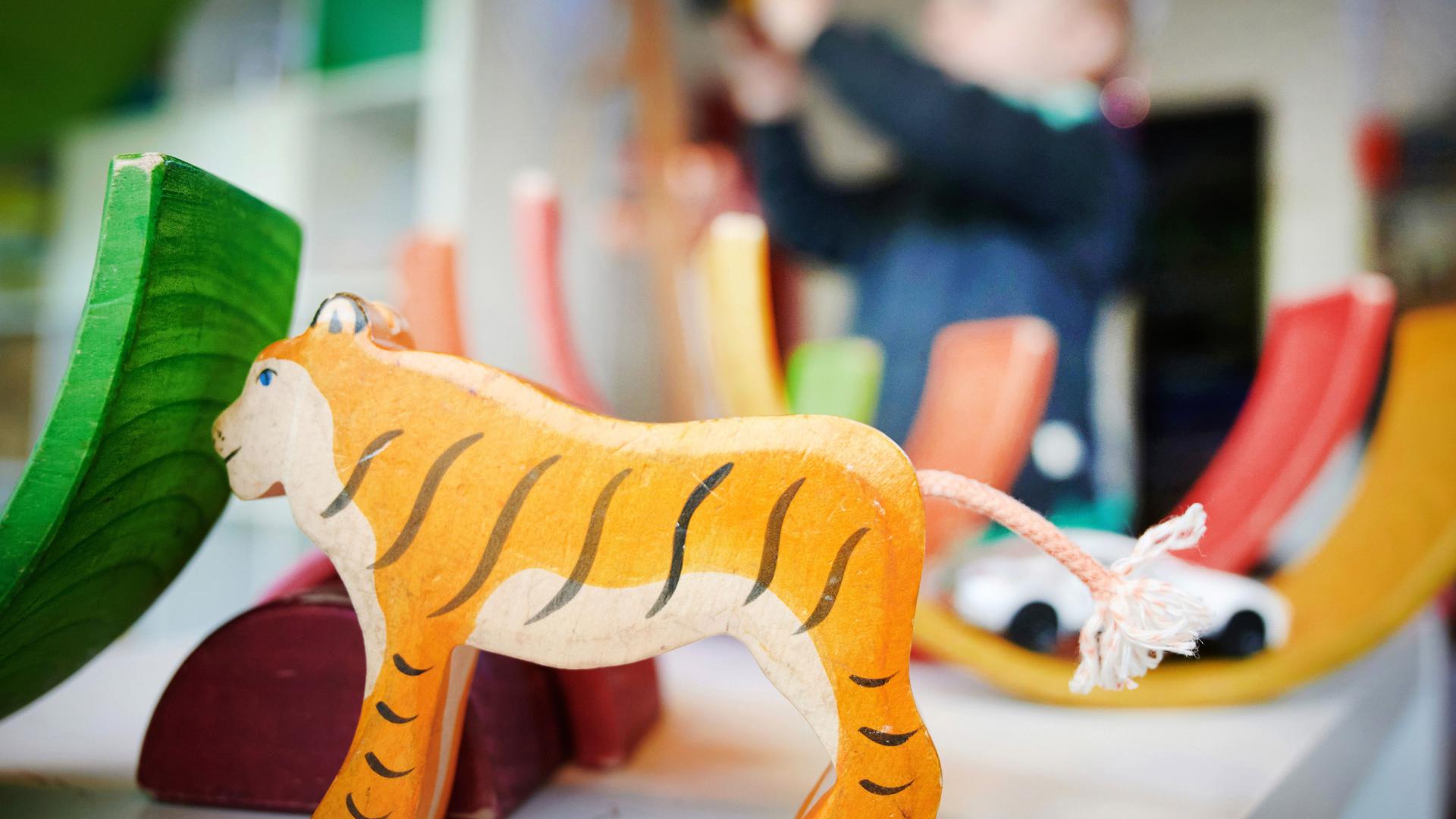 Ein Junge spielt in einer Kindertagesstätte hinter einer Tigerfigur mit Bauklötzen und einem Spielzeugauto.