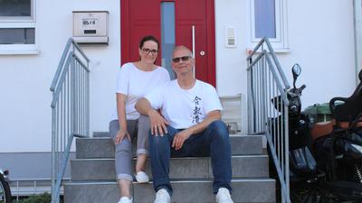 Daniela und Stephan Linke sitzen auf einer Treppe vor einer roten Haustür