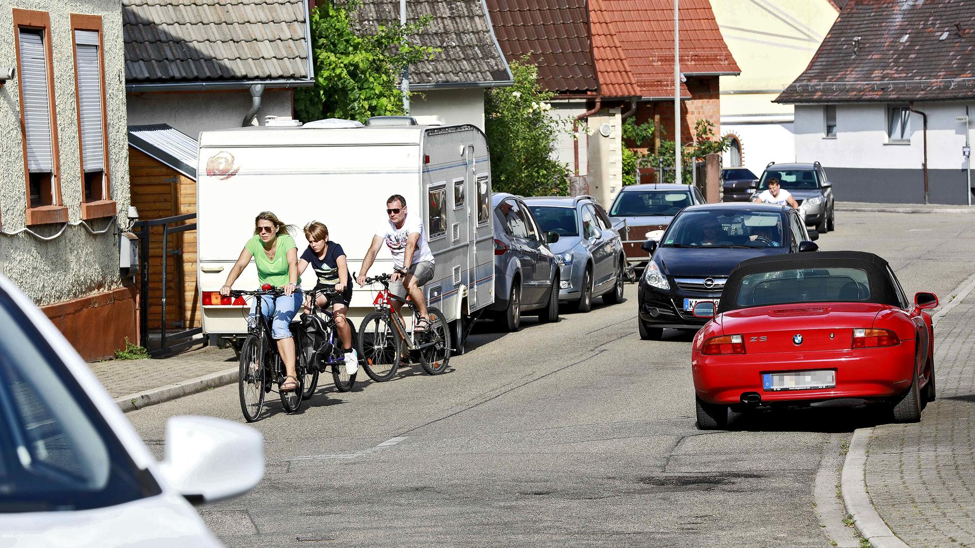 Fahrende Autos, Radfahrer, parkende Fahrzeuge in der Weingartener Straße in Jöhlingen