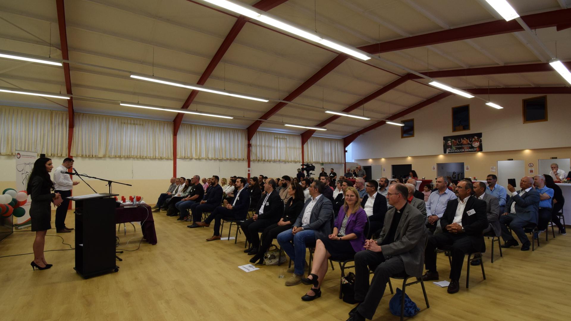 Gäste hören bei der Eröffnung des neuen Gemeindehauses der Alevitischen Gemeinde den Moderatoren der Veranstaltung zu.