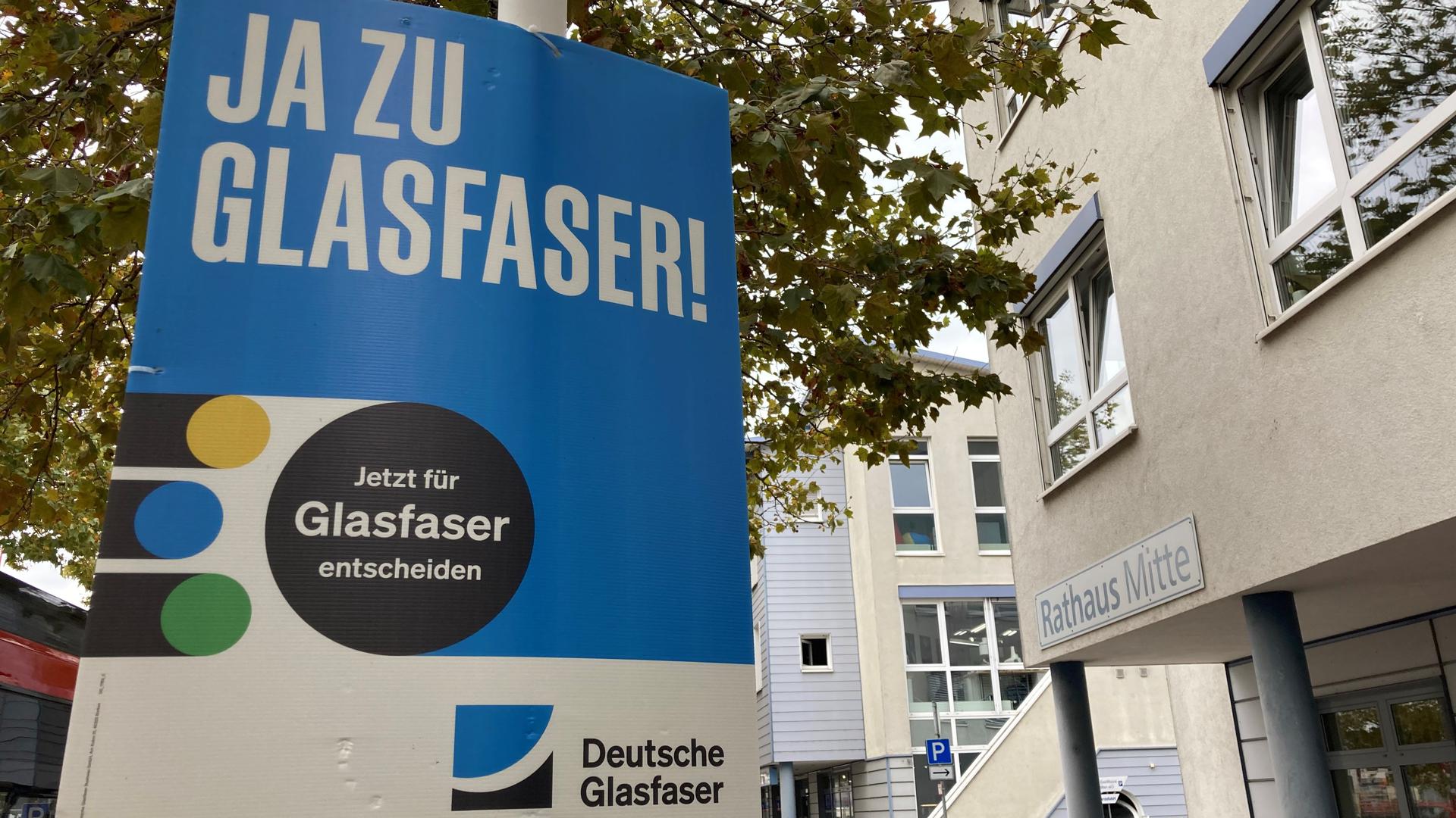 Ein Werbeplakat der Deutschen Glasfaser hängt an einem Schild vor dem Rathaus Rheinstetten. „Ja zu Glasfaser! Jetzt für Glasfaser entscheiden“ steht darauf.