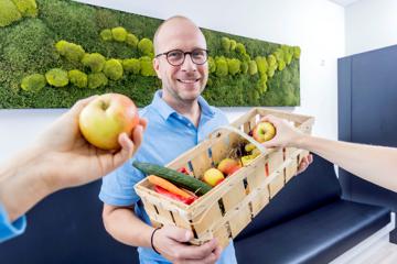Dr. Philipp Hoffmanns im Wartezimmer vor der Moowand mit Obstkorb