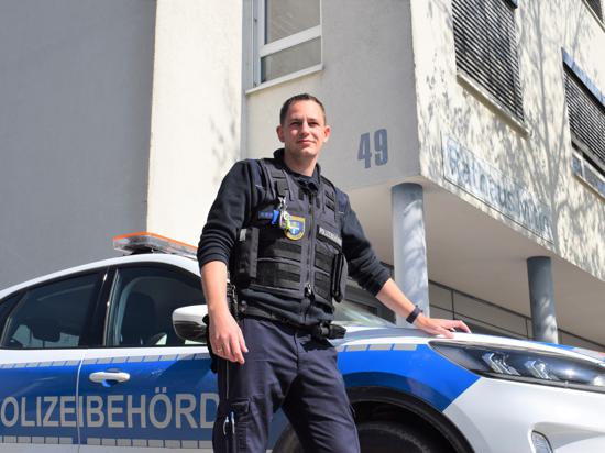 Lucas Mayer vom Ordnungsamt Rheinstetten steht vor einem Dienstfahrzeug mit der Aufschrift Polizeibehörde.