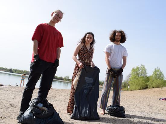 Janek, Marla und Paul stehen mit Müllsäcken am Ufer des Epplesees in Rheinstetten.