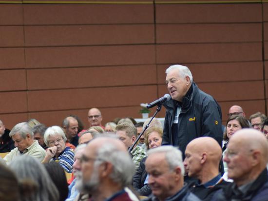 Ein Mann aus dem Publikum steht bei der OB-Kandidatenvorstellung in der Keltenhalle Mörsch am Mikrofon.