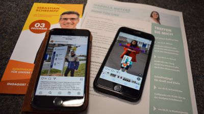 Wahlflyer und Anzeigen liegen neben Handys, die die Instagram-Profile von Isabella Metzke und Sebastian Schrempp zeigen.