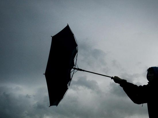 Ein Regenschirm einer Fußgängerin wird von einer Windböe erfasst.