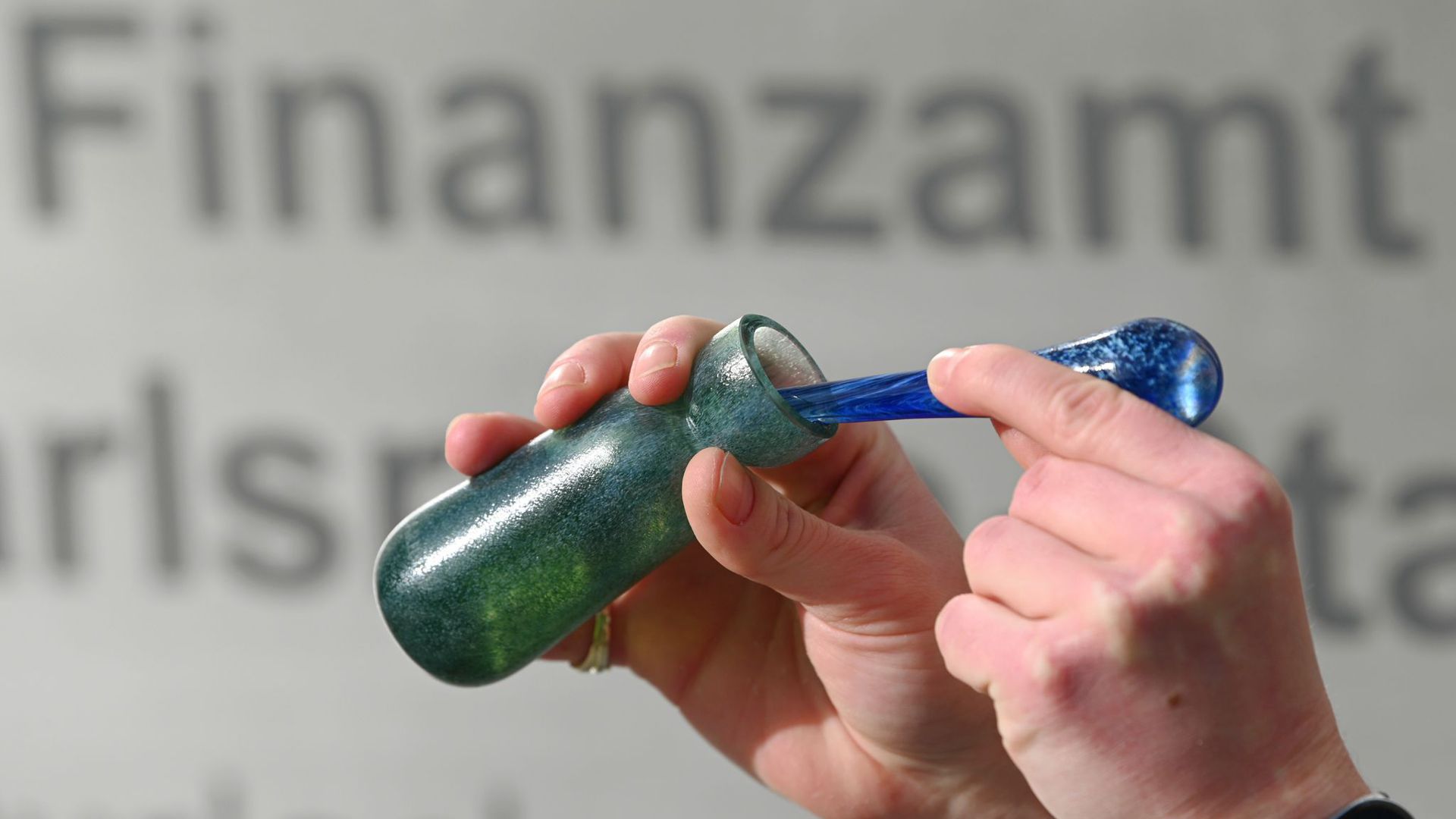 Ein Mann hält vor dem Karlsruher Finanzamt einen Flakon mit Banknoten-Duft, das Parfüm „Aerarium“, in der Hand.