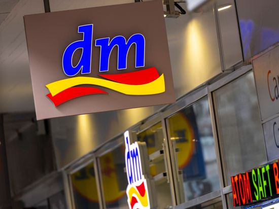 Ein beleuchtetes Logo der Drogeriekette „dm“ hängt über dem Eingang zu einem Geschäft.