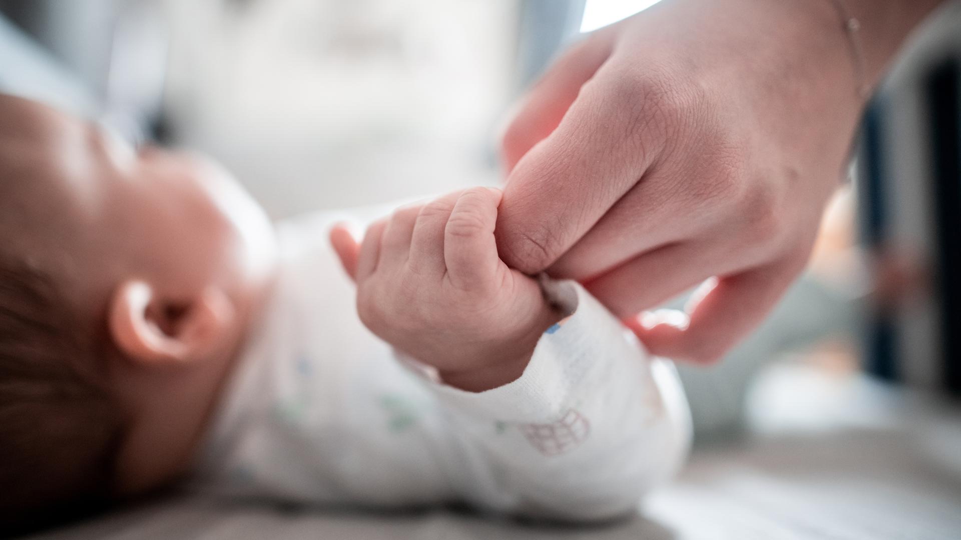 Ein Baby klammert sich an die Finger seiner Mutter. 