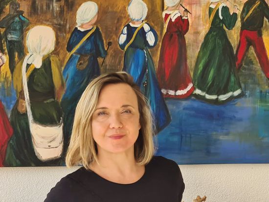 Katja Seebach vor einem selbst gemalten Gemälde, das Frauen in mittelalterlicher Tracht zeigt. 