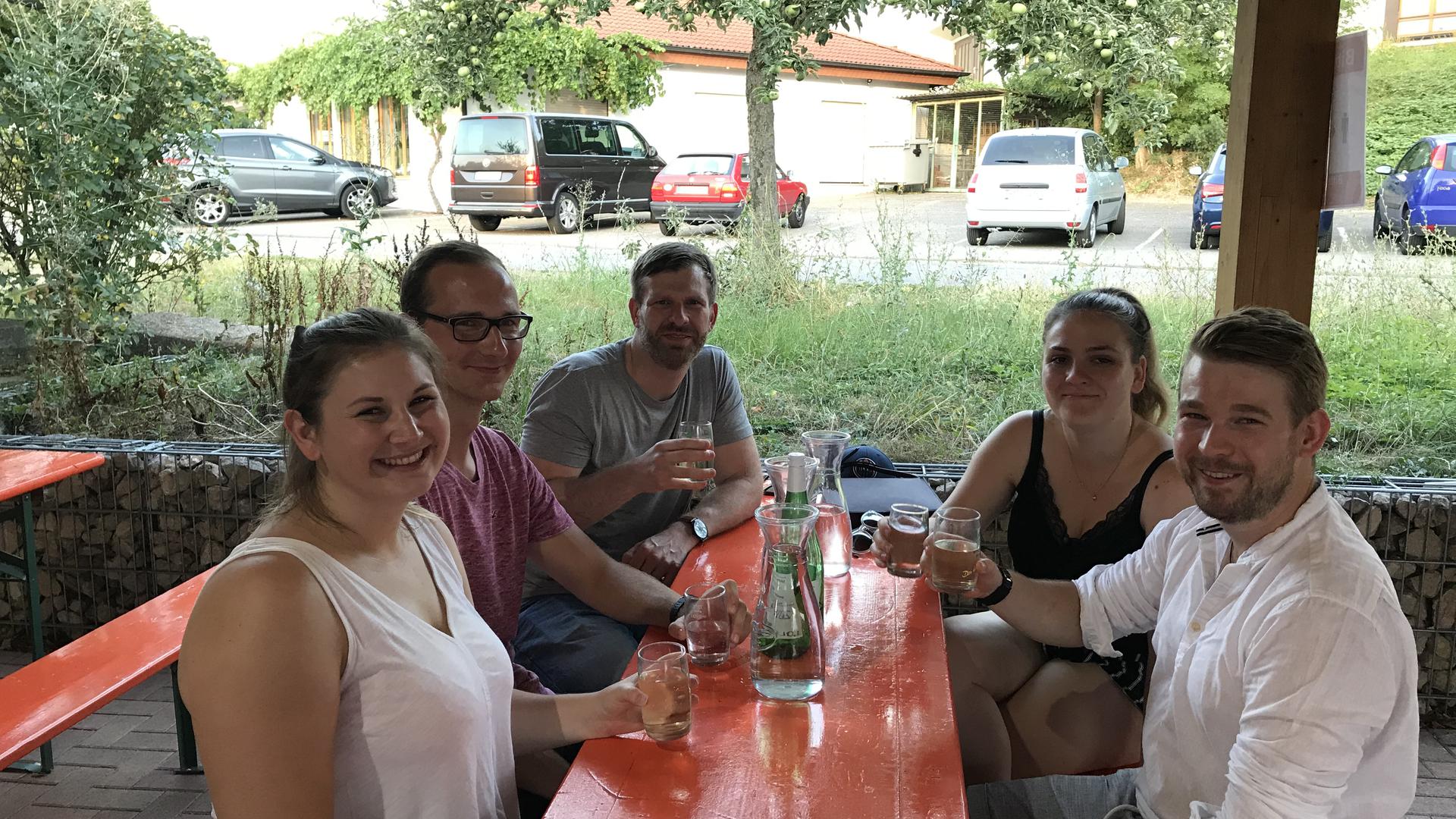 Eine Gruppe junger Menschen sitzt auf Bierbänken und trinkt Weinschorle in der Winzerrast in Wiesloch.