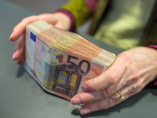 Eine Bank-Mitarbeiterin hält am Schalter einer Sparkasse in München 5000 Euro in 50-Euro-Scheinen in den Händen.