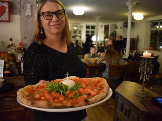 Arcangela Lamola Vedda, Inhaberin des Restaurants La Piazzetta in der Brettener Melanchthonstraße, hält einen Teller mit einer Pizza in die Kamera und lächelt. 