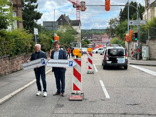 VBU-Vorsitzender Jörg Biermann (links) und Bürgermeister Michael Nöltner zeigen die Schilder, die zum Sporgassenparkplatz führen. Derweil fährt ein Autofahrer rückwärts aus der Heilbronner Straße heraus, weil er den Hinweis auf die gesperrte Straße übersehen hat.