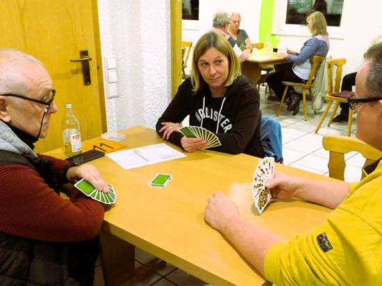 Drei Personen spielen an einem Tisch Karten
