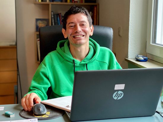 Ein Mann in einem grünen Kapuzenpullover sitzt an seinem Laptop. 