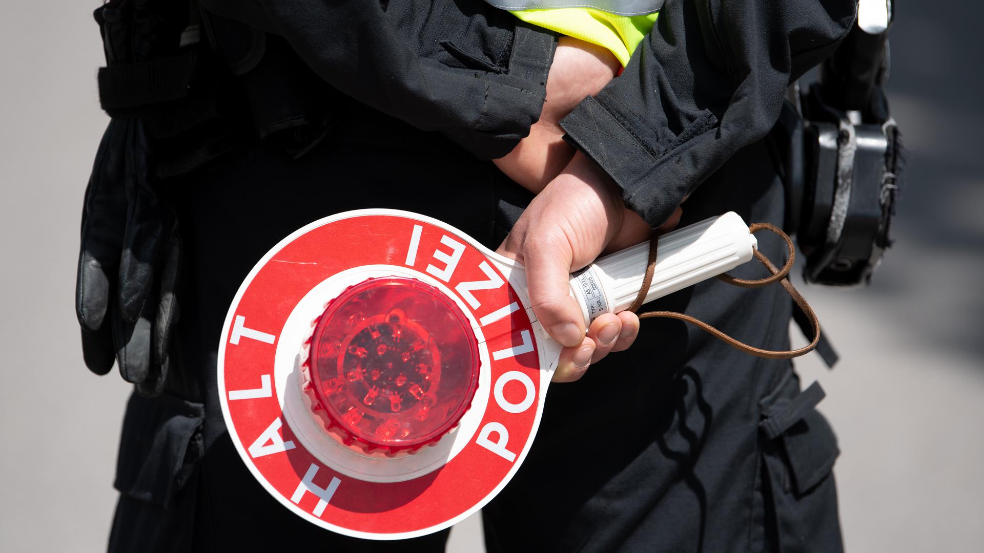 Ein Polizist hält eine Kelle mit der Aufschrift „Halt“ in den Händen.