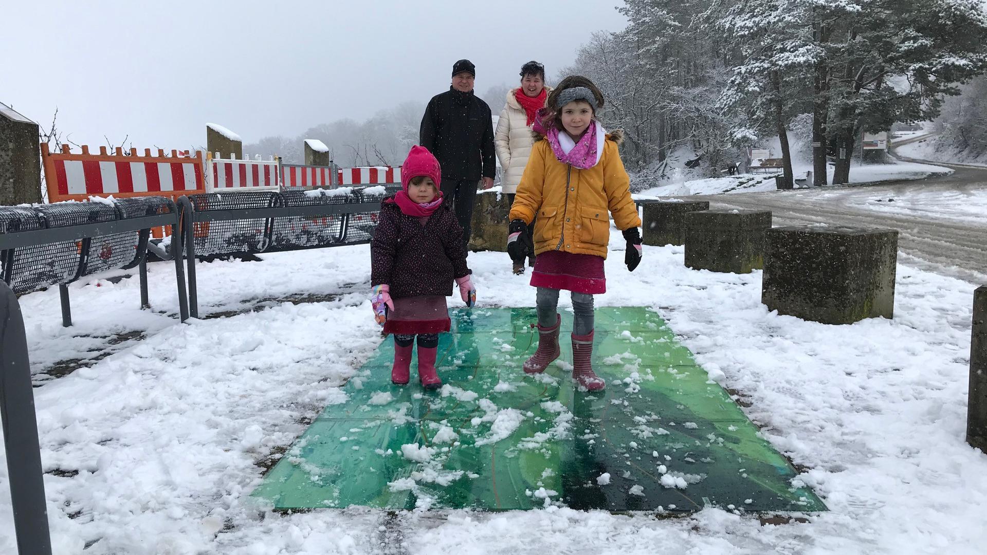 Zwei Mädchen schlittern über eine in den Weg eingelassene Glasfläche, die vom Schnee rutschig ist.  