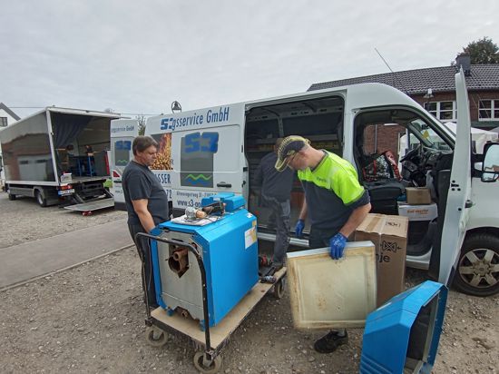 Zwei Handwerker laden Geräte in einen Lieferwagen.