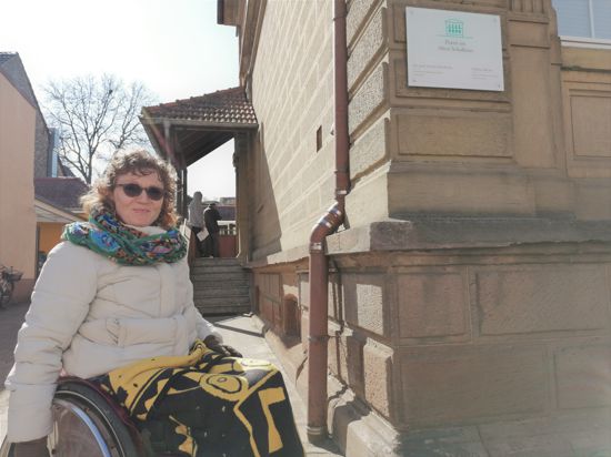Frau im Rollstuhl vor Gebäude mit Treppe