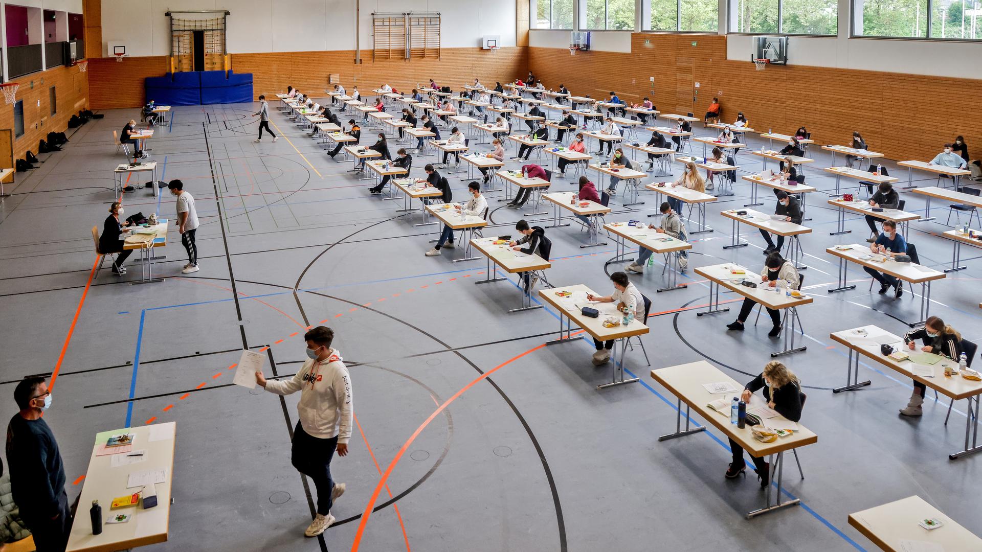 Mehrere Schüler sitzen an Schreibtischen in einer Sporthalle