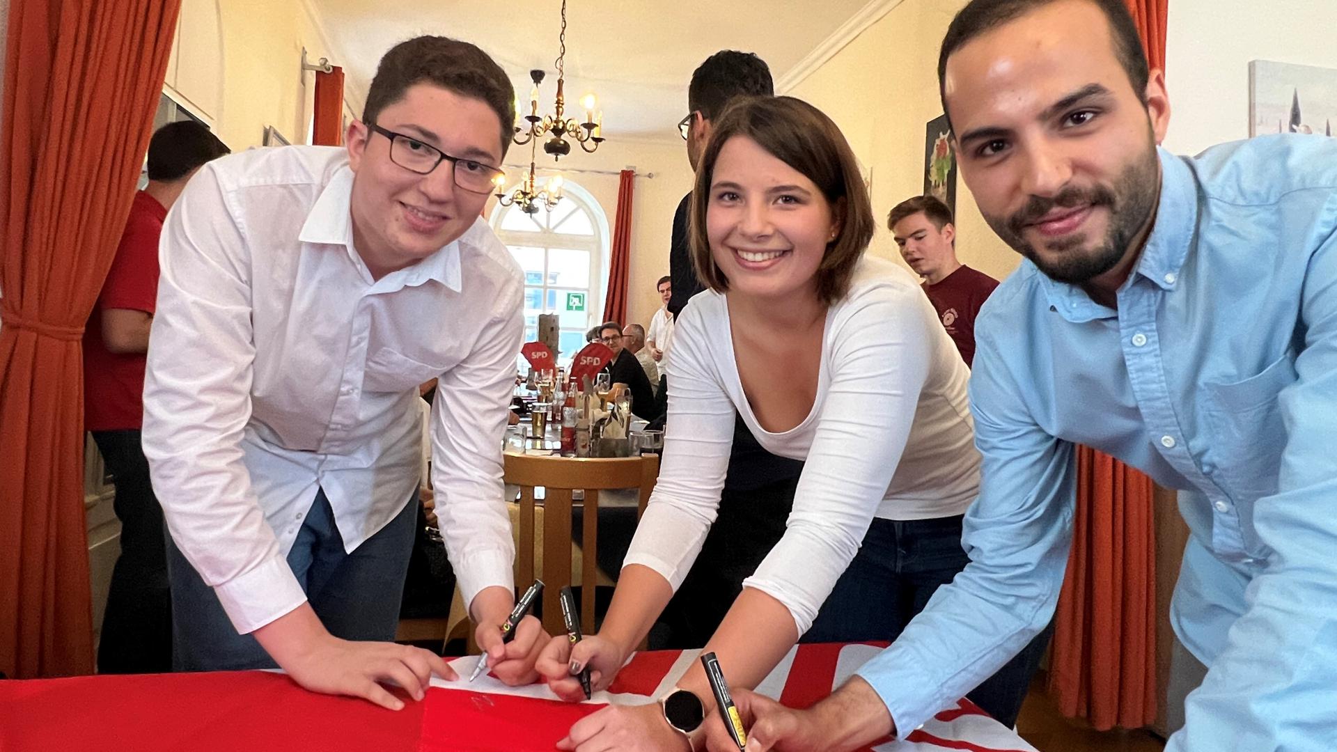 Nael Essafi, Magdalena Backes und Can Yildirim (von links) unterschreiben als Erste auf einer Flagge der SPD. Seit Mittwochabend bilden sie zusammen den Vorstand der Brettener Juso AG.