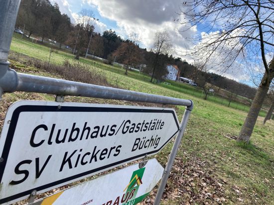Ein Straßenschild zeigt zum Clubhaus des SV Kickers Büchig. Im Hintergrund sieht man eine grüne Wiese.