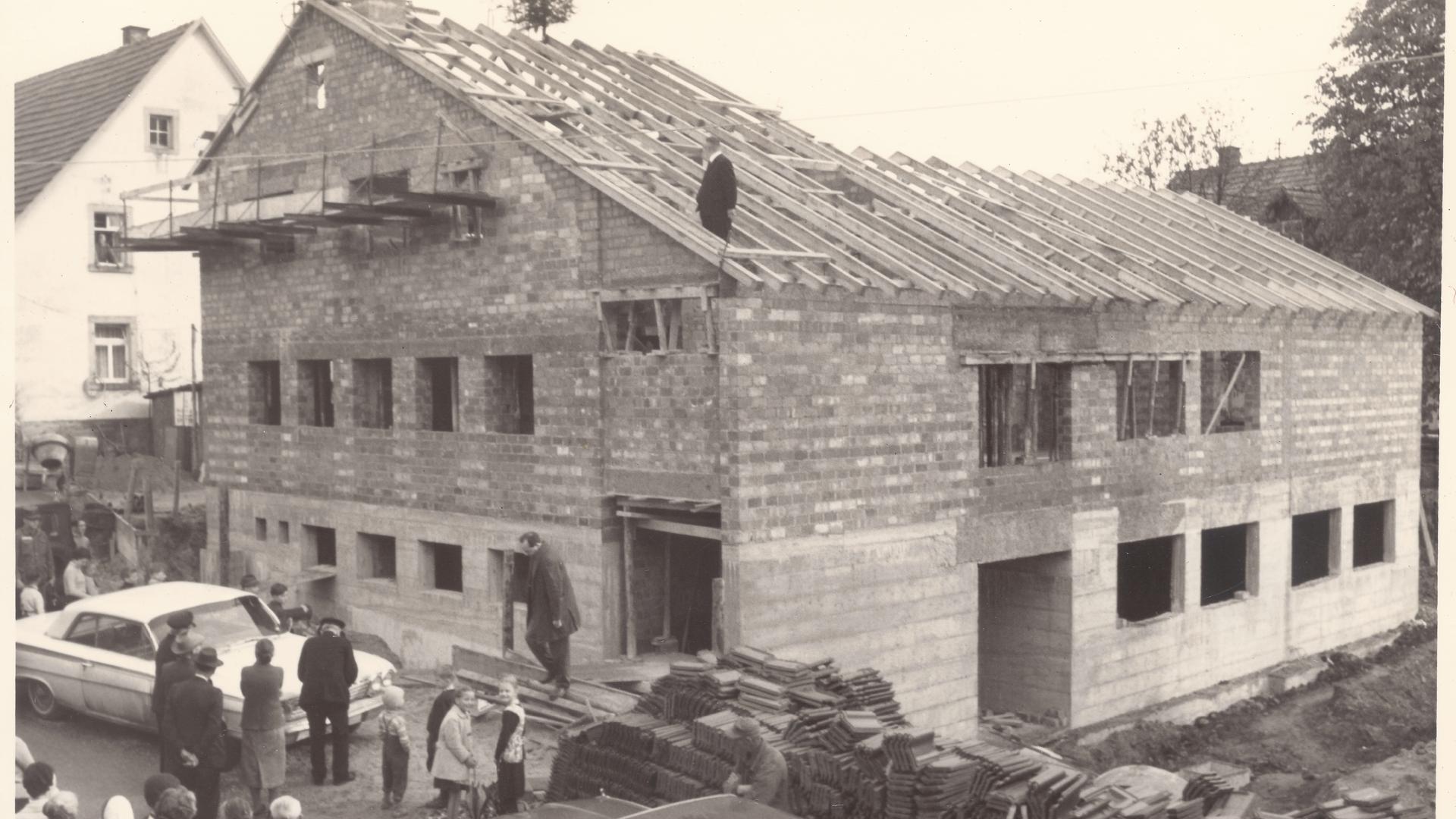 Das Bild zeigt den Kindergarten-Rohbau in Ruit von 1965. Auf dem Dach ist der damalige Ruiter Pfarrer Haas beim Richtfest zu sehen.