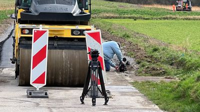 Ein Kameramann des Filmteams platziert mehrere Kameras auf dem Brettener Teil des Feldwegs. Zur selben Zeit laufen Asphaltarbeiten.