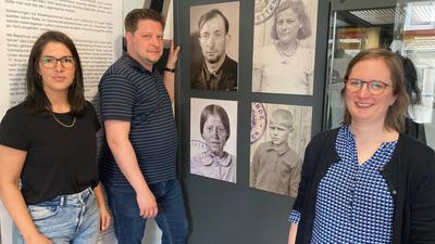 Drei Personen vor historischen Porträtfotos