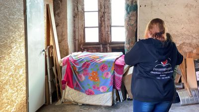 Zwei Frauen schauen den Schlafplatz von Obdachlosen in einer Scheune an.