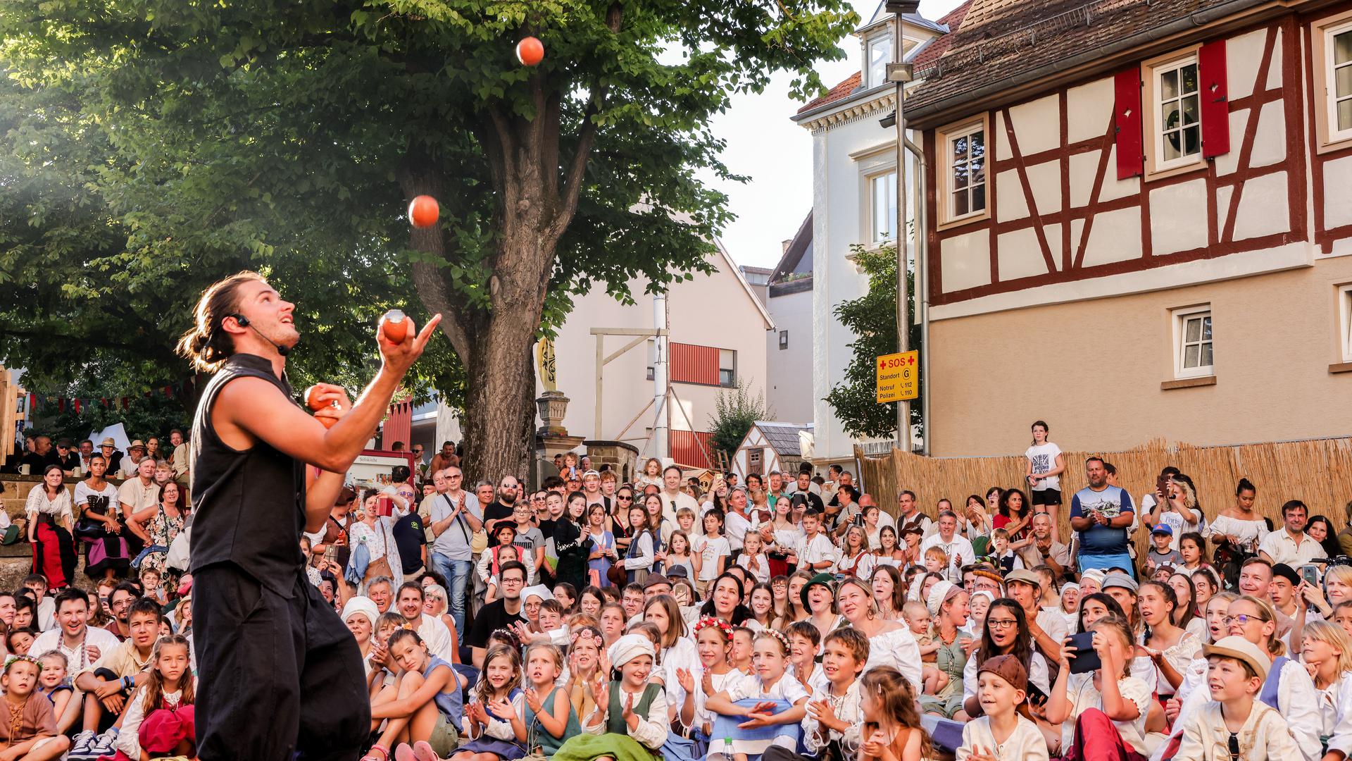 Ein Mann jongliert mit Bällen und viele Kinder und Erwachsene schauen mit offenem Mund zu.