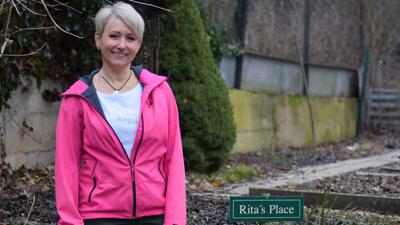 Rita Eberl steht in ihrem Garten neben dem Schild „Rita’s Place“