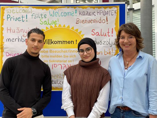 Ein junger Mann aus Afghanistan, eine junge Frau aus Syrien und ihre ehemalige Lehrerin stehen nebeneinander im Foyer der Schillerschule Bretten.