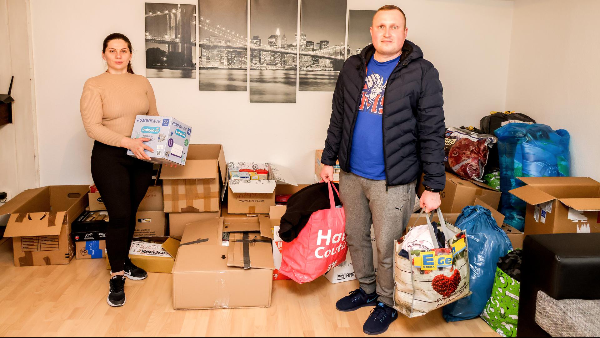 Ein junges Ehepaar sammelt Kartons in seinem Wohnzimmer, um Spenden in die Ukraine zu bringen. 