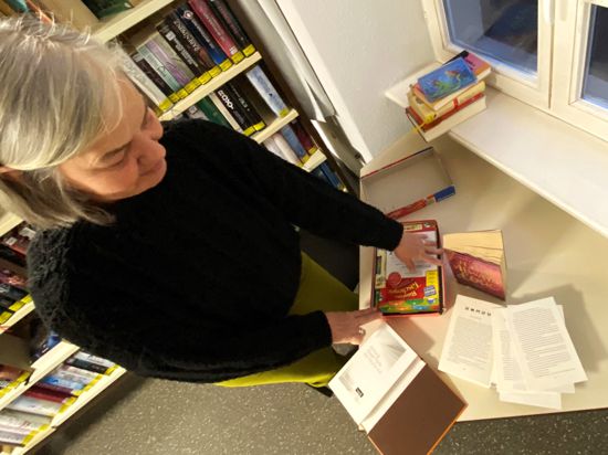 Eine Büchereimitarbeiterin zeigt Bücher und Spiele in der Stadtbücherei, die beschäfigt zurückkamen.