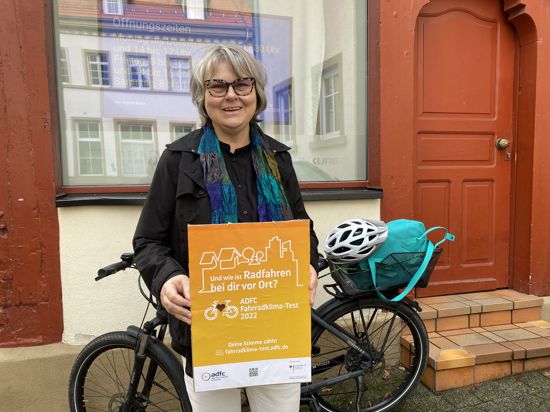 Jutta Biehl-Herzfeld, Sprecherin des adfc in Bretten, steht vor ihrem Fahrrad und hält ein Werbe-Plakat für den Fahrradklimatest in ihren Händen.