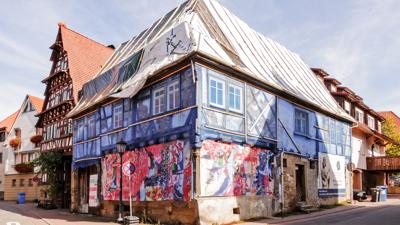 Ein großes Fachwerkhaus steht an einer Straßenecke in Oberderdingen. Sein Fachwerk wird von einem blauen Netz umspannt. Auf dem Dach liegt eine Folie statt Ziegeln.  